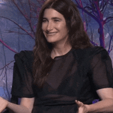 a woman in a black dress is smiling and raising her arms in the air