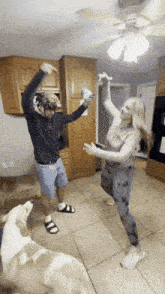 a man and woman are dancing in a kitchen with a dog watching
