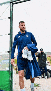 a man in a blue adidas jacket is carrying a pair of white sneakers