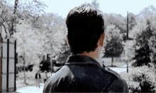 a man in a black leather jacket is standing in front of a gate .