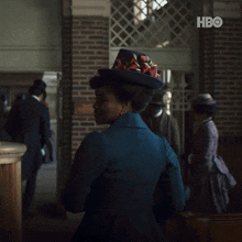 a woman in a blue hat is standing in front of a brick wall with hbo written on it