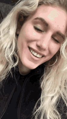 a woman with blonde hair and hoop earrings smiles