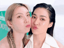 a woman kisses another woman on the cheek in front of a sign that says 00