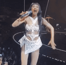 a woman in a white dress is singing into a microphone on stage