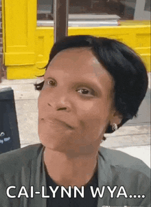 a woman is making a funny face in front of a yellow building and says cal-lynn wya .