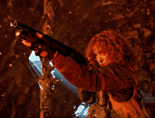 a woman with curly hair is holding a gun in a dark room
