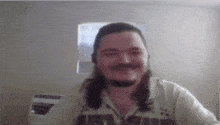 a man with long hair and a beard is smiling in a room .