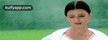 a woman in a white shirt is standing in front of a green background and making a funny face .