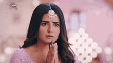 a woman wearing a maang tikka and a necklace is praying