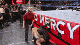 a woman is kneeling on the ground in front of a sign that says mercy .