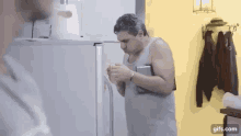 a man in a tank top is standing in front of a fridge .