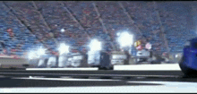 a blue car is driving down a race track in front of a stadium .
