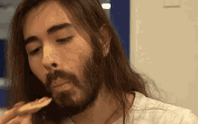 a man with long hair and a beard eating a piece of food