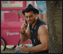 a man leaning against a tree talking on a cell phone in front of a pink popcorn machine