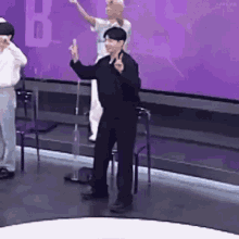 a man in a black suit is giving a peace sign on a stage .