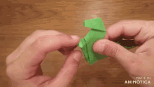 a person is holding a green origami piece with the words made in animotica below it