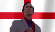 a man in a suit and tie stands in front of a red and white cross