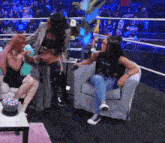 a group of women are sitting on a couch in a wrestling ring talking to each other