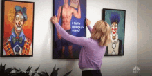 a woman is hanging a painting of a clown on the wall .