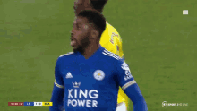 a soccer player wearing a blue jersey with the word king on it is standing on a field .