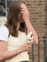 a woman is covering her face while holding an ice cream cone in front of a brick building .