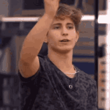 a young man in a black t-shirt is raising his hand in the air .