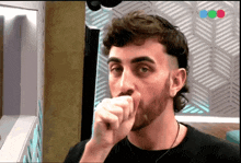 a man with a beard is covering his mouth with his hand in front of a wall with a chevron pattern