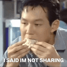 a man is eating a sandwich with the words `` i said im not sharing '' written on it .