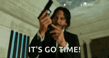 a man in a suit is holding a gun in his hand and saying `` it 's go time '' .