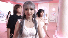 a girl with gray hair is standing in a pink room with other girls