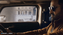 a man wearing sunglasses is driving a car with the twitter username pranay_varma below him