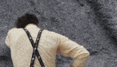 a man wearing a yellow shirt and suspenders is standing in front of a rock