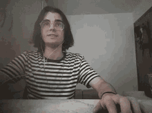 a young man wearing a striped shirt and glasses is sitting at a table