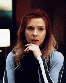 a woman with red hair is sitting with her hand on her chin and looking at the camera