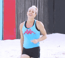 a woman wearing a blue kappa tank top is running on a beach
