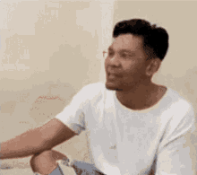 a man wearing a white shirt and ripped jeans is sitting down