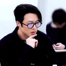 a young man wearing glasses and a black jacket is sitting at a table .