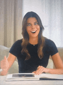 a woman in a black shirt is smiling while sitting at a table with a book