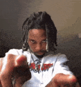 a man with dreadlocks is pointing at the camera with his hands .