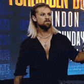 a man with long blonde hair and a beard is standing in front of a sign that says london sunday .