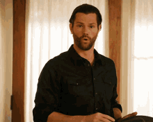 a man with a beard is standing in front of a window