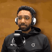 a man wearing headphones and a black jacket stands in front of a microphone .