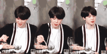 a young man is sitting at a table eating food with chopsticks ..