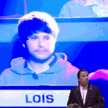 a man in a suit stands in front of a screen that says lois on it