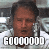 a man wearing headphones is sitting in front of a microphone and saying `` good '' .