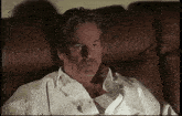 a man in a white shirt is sitting on a brown couch