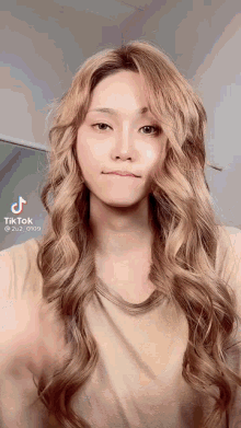 a woman with long blonde hair is wearing a beige shirt and making a funny face .