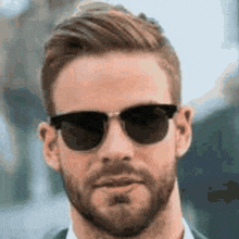 a man with a beard is wearing sunglasses and a suit .