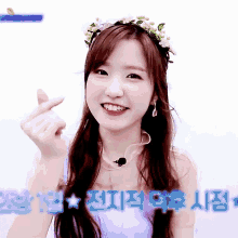 a girl with a flower crown on her head is smiling and making a heart shape with her fingers