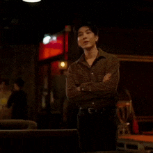 a young man in a plaid shirt is standing in a dark room with his arms crossed .